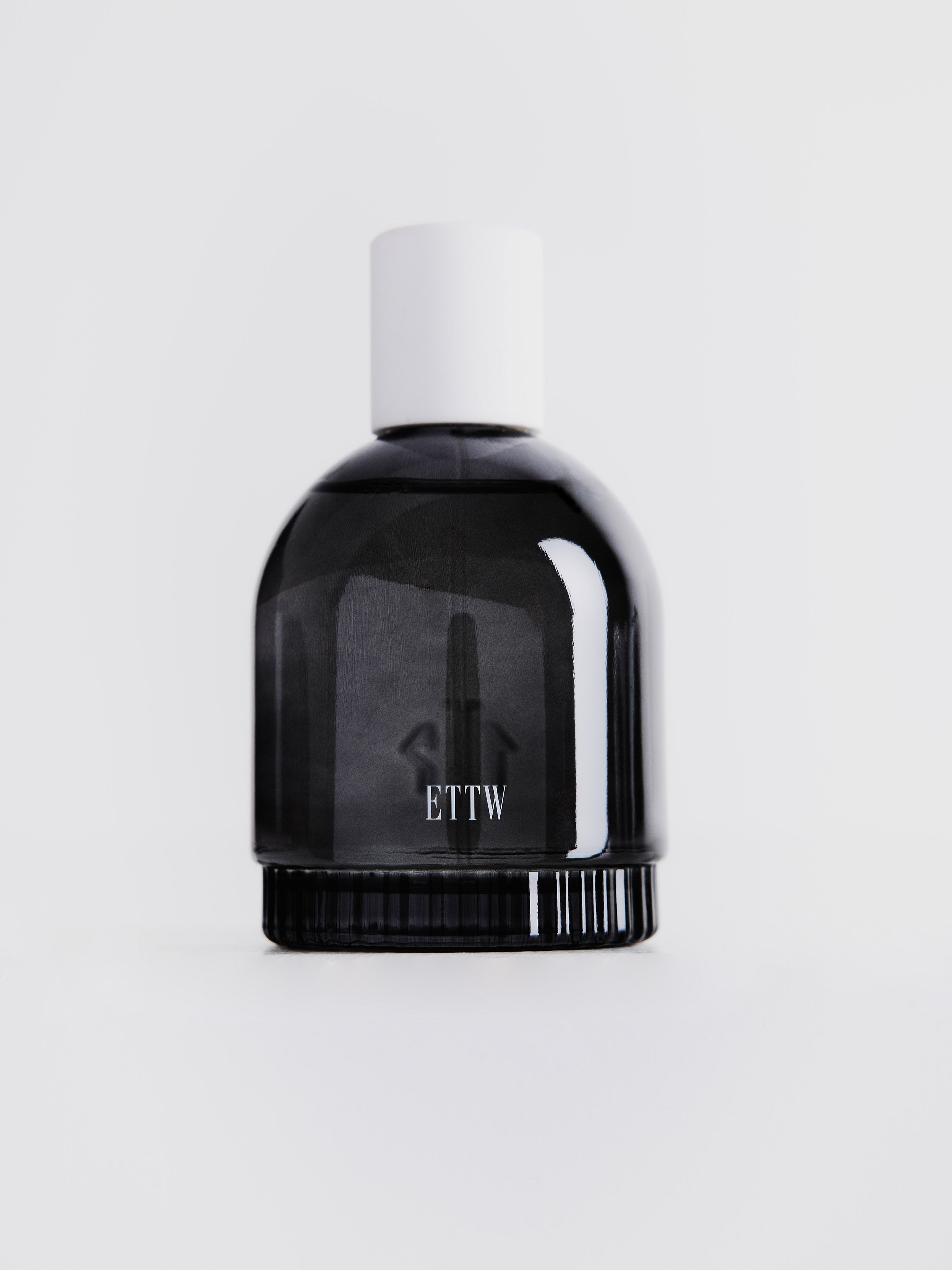 Small dark gray transparent perfume bottle with white "ETTW" label and white cap on top