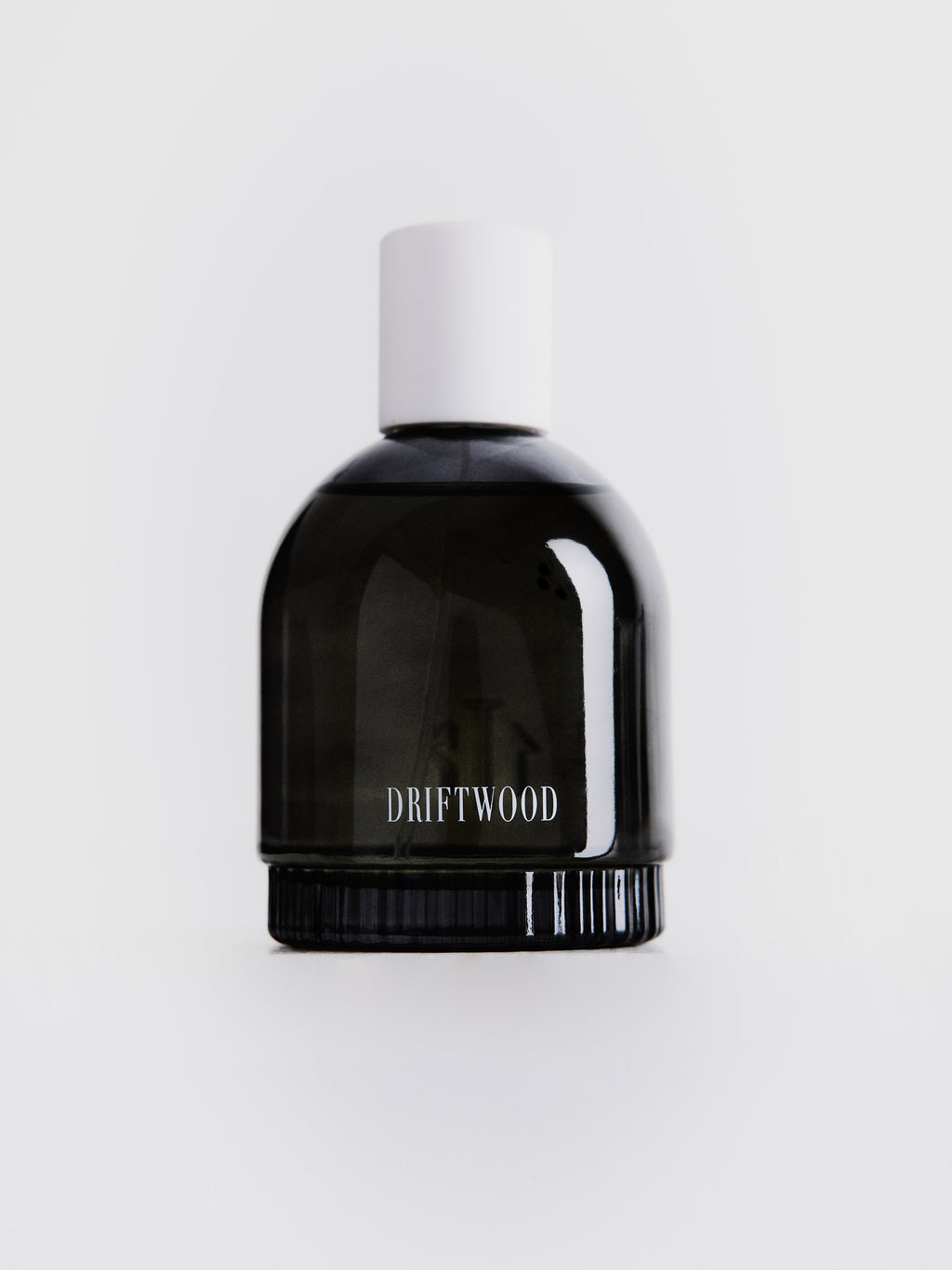 Small dark gray transparent perfume bottle with white "DRIFTWOOD" label and white cup on top 